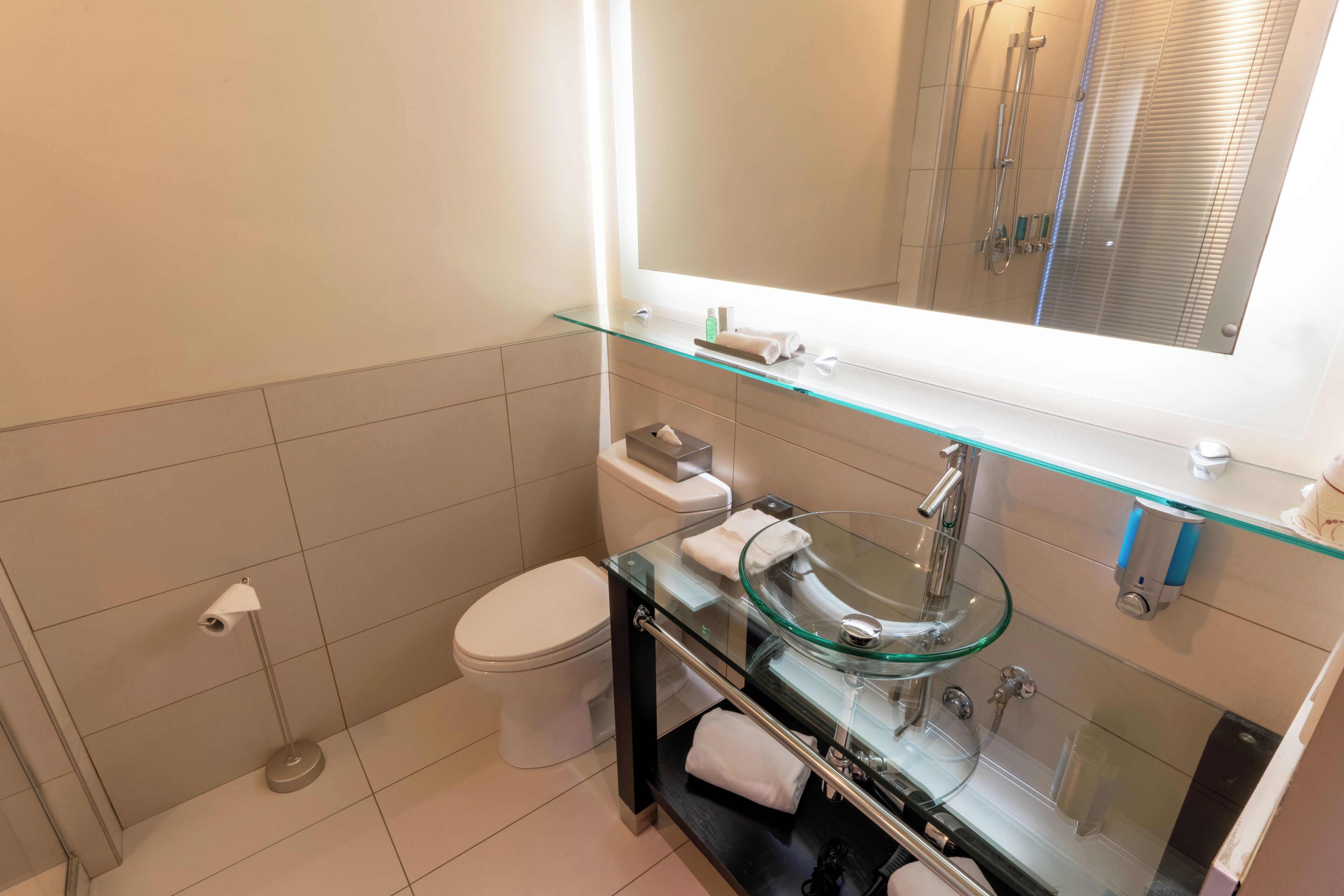 Un baño moderno con un lavabo de vidrio, un inodoro y una ducha.