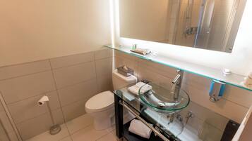 A modern bathroom with a glass sink, a toilet, and a shower.