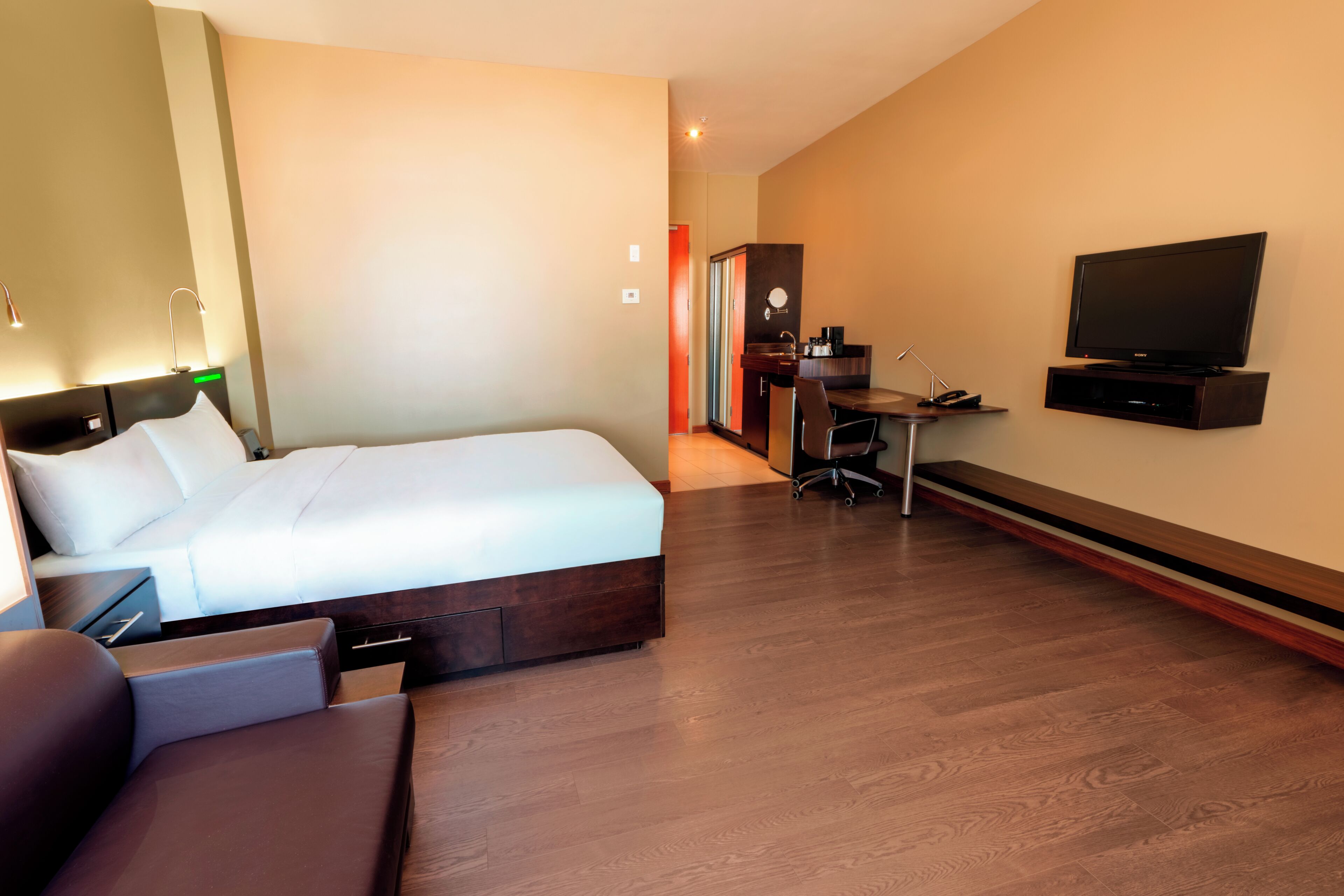 Una camera d'albergo con un letto, una televisione, una scrivania con una sedia e un angolo cottura.