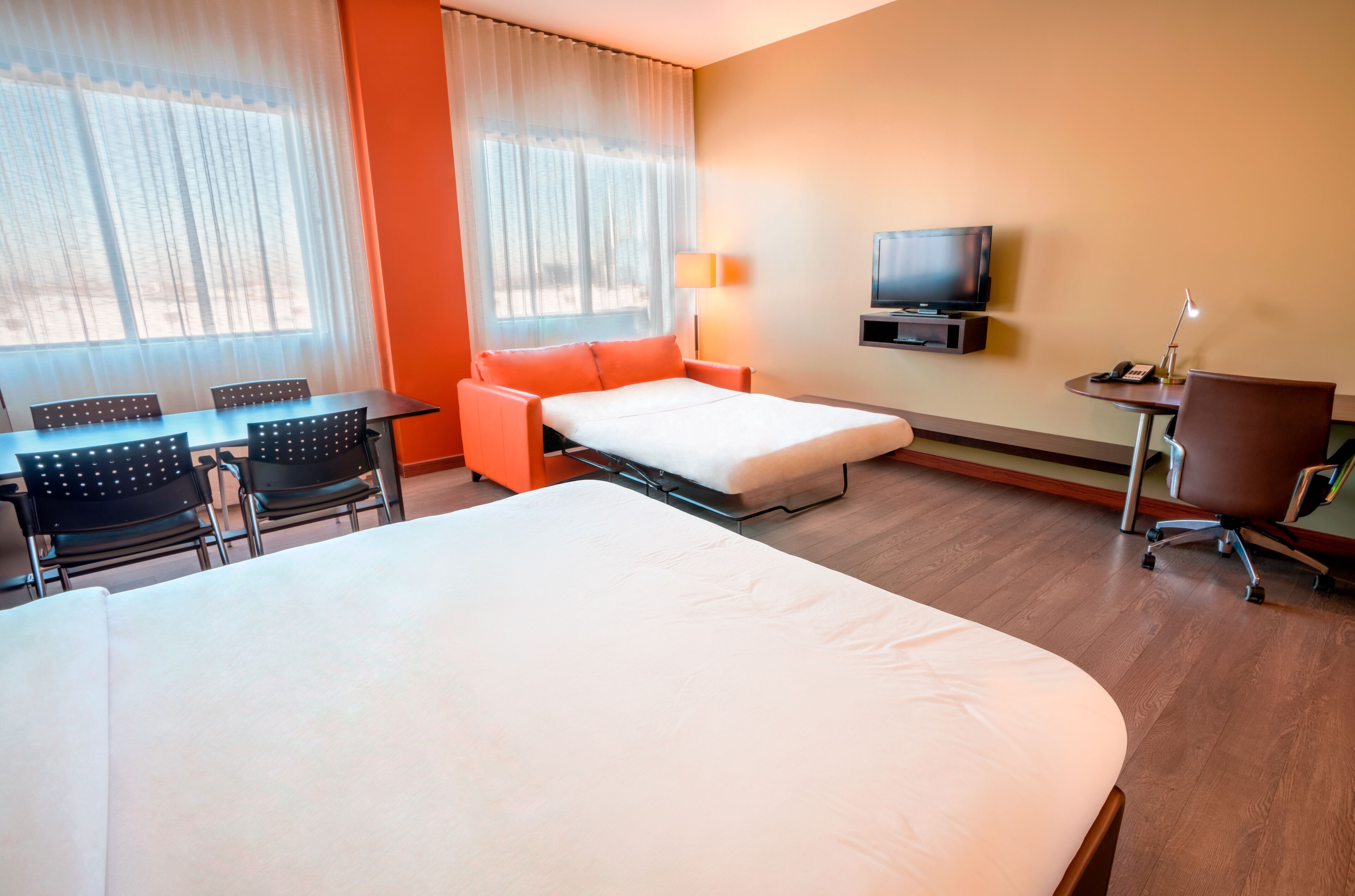A hotel room with a bed, a desk, a chair, a TV, and a lamp.