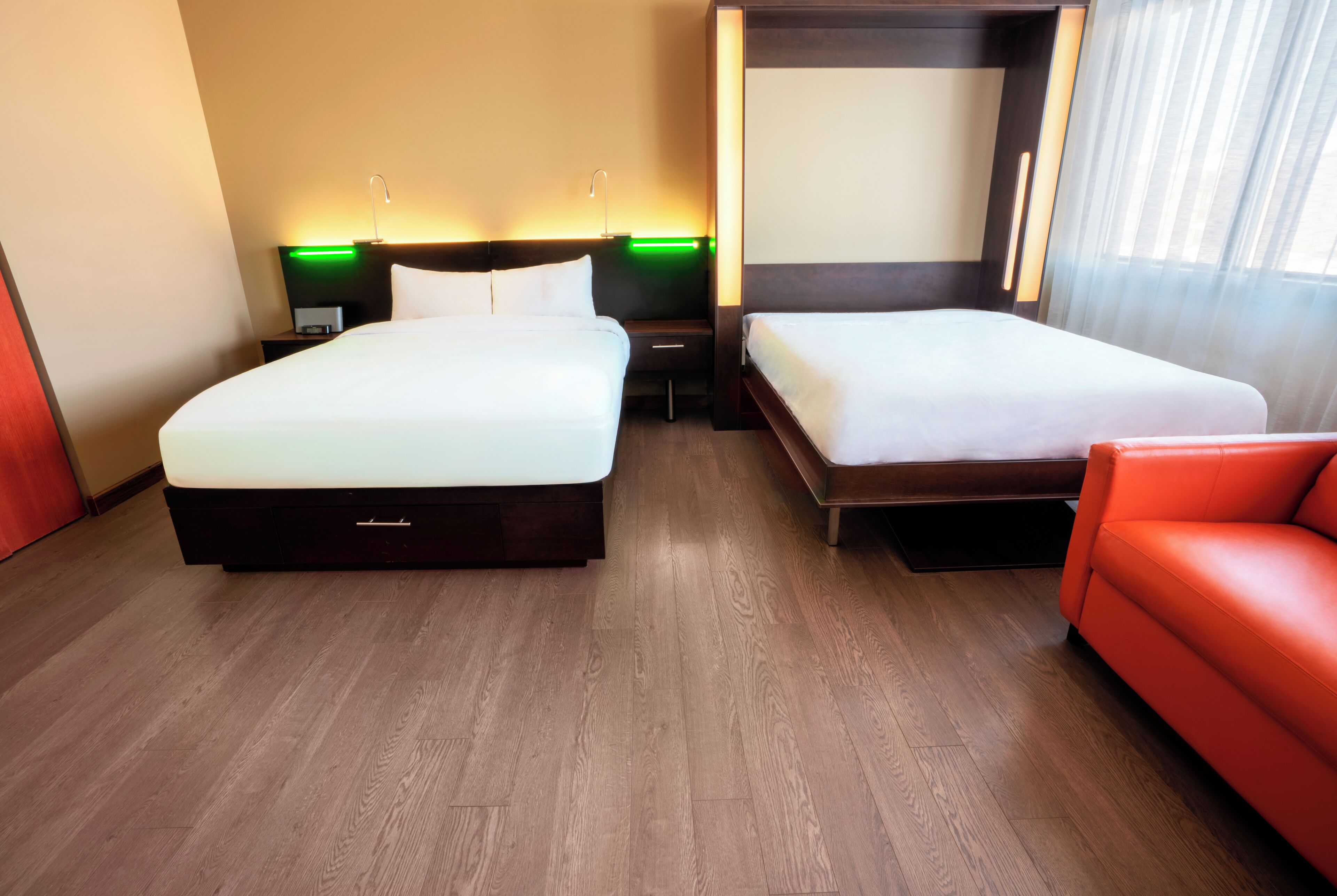 Una habitación de hotel con dos camas, un sofá rojo y una mesita de noche con lámpara.
