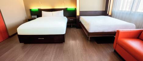 Una habitación de hotel con dos camas, un sofá rojo y una mesita de noche con lámpara.