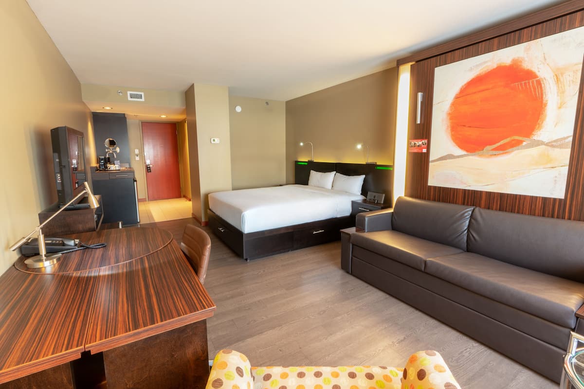 Una habitación de hotel con cama, sofá, escritorio y un cuadro abstracto grande en la pared.