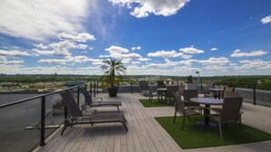 Una terraza en la azotea con sillones, mesas y una palmera.