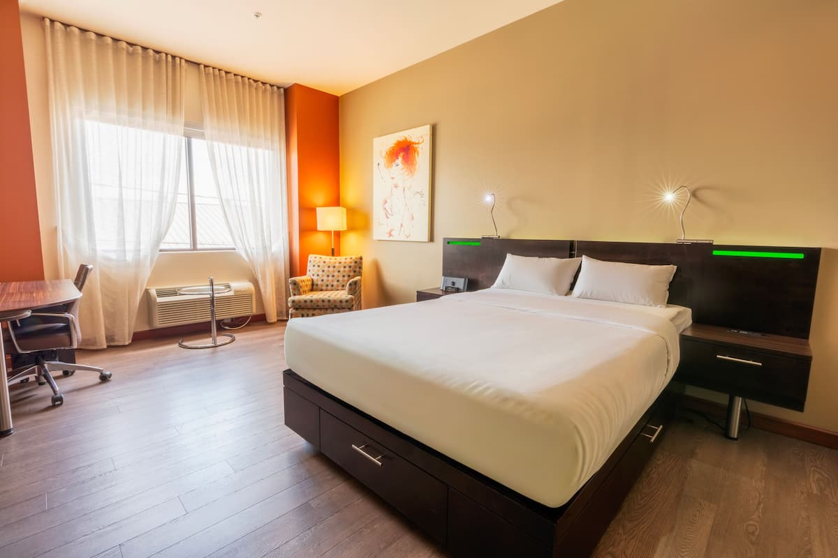 Habitación de hotel con cama, mesitas de noche, escritorio, silla y ventana con cortinas.
