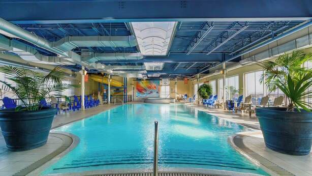 Una piscina interior con agua cristalina, rodeada de sillas de descanso y plantas en macetas.