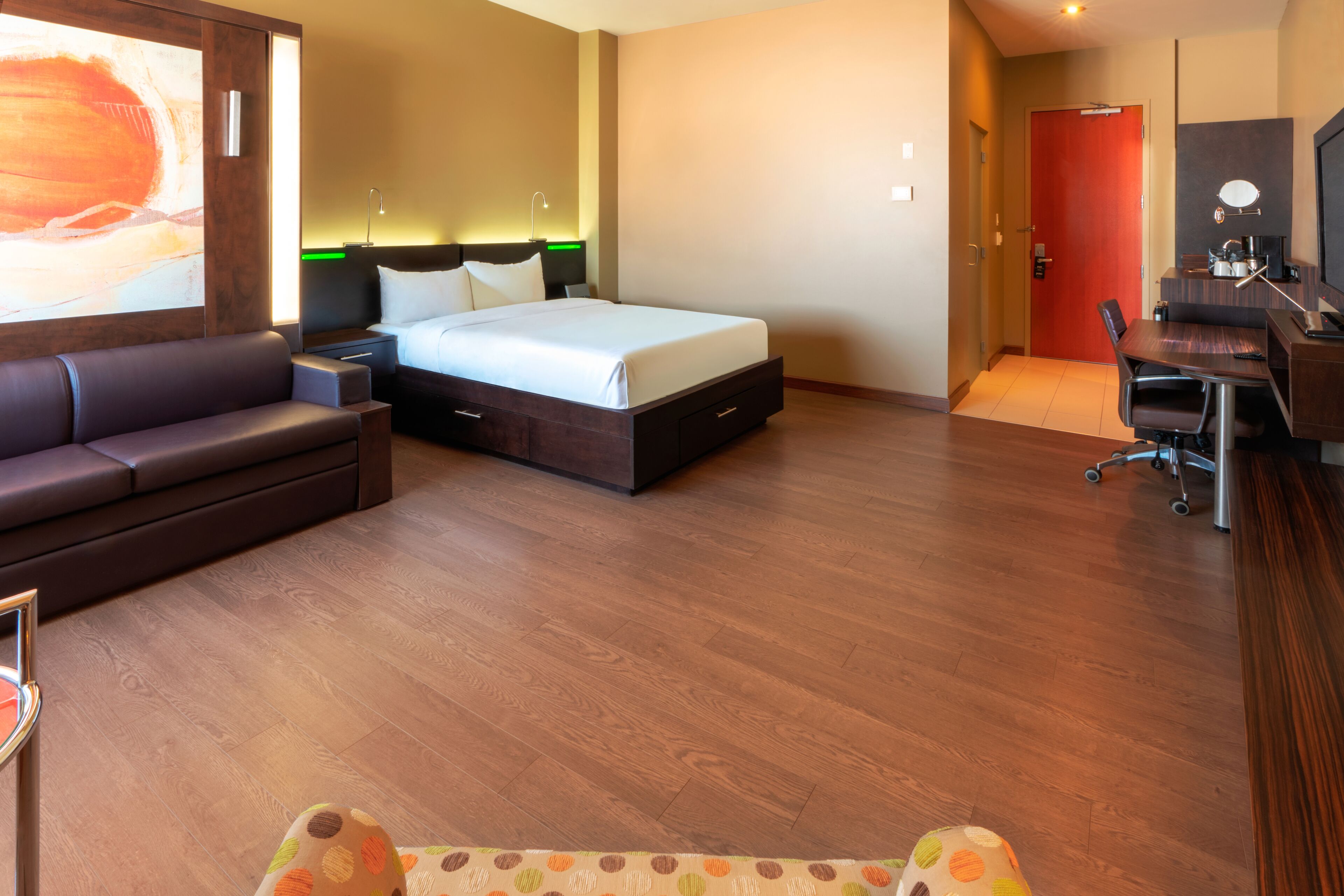 Habitación de hotel con cama, escritorio, silla, sofá y un cuadro grande en la pared.