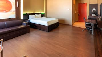 Ein Hotelzimmer mit Bett, Schreibtisch, Sessel, Sofa und einem großen Gemälde an der Wand.