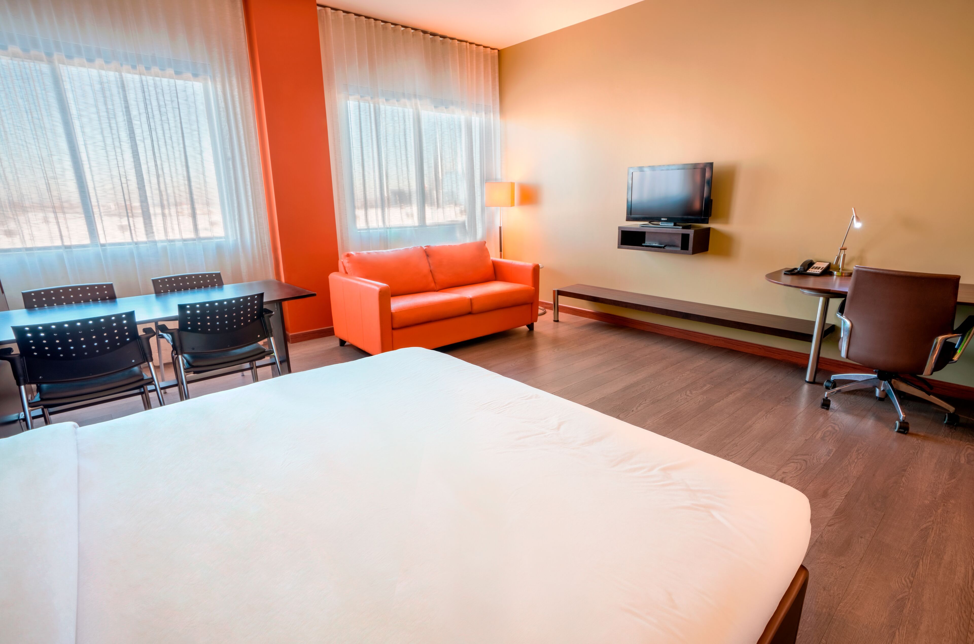 A hotel room with a bed, a sofa, a TV, a desk with a lamp, and a chair.