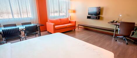 A hotel room with a bed, a sofa, a TV, a desk with a lamp, and a chair.