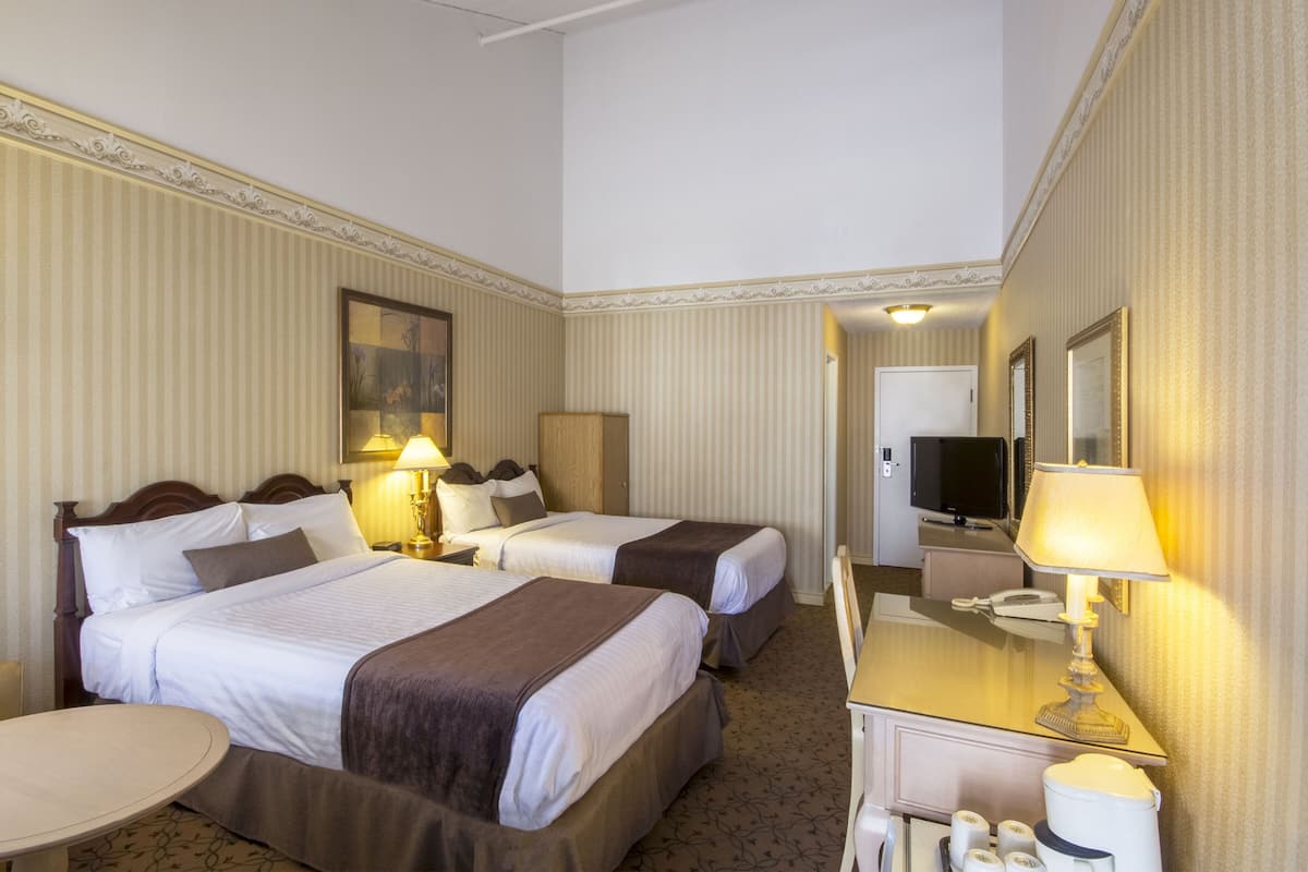 A hotel room with two beds, a desk with a lamp, a television, and a mirror.