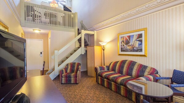 A cozy living room with a sofa, armchairs, a TV, and a staircase leading to an upper level. - Auberge Québec (Québec City)
