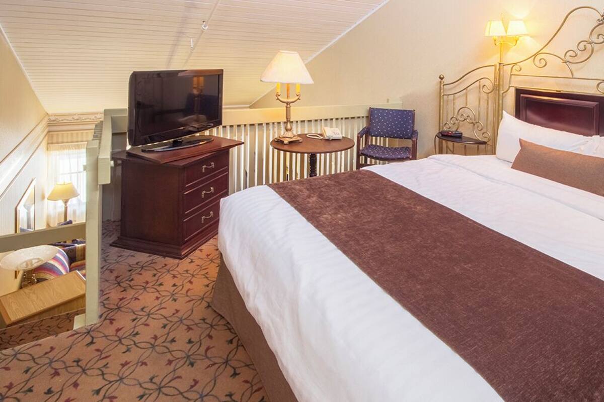 A hotel room with a large bed, a television on a dresser, a chair, and a lamp.