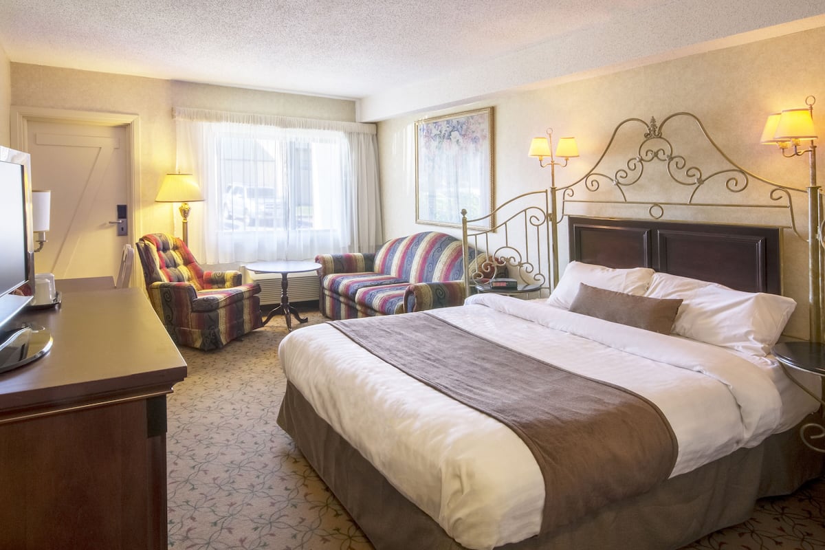 A hotel room with a large bed, two armchairs, a small table, and a desk with a lamp.