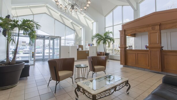 Um hall espaçoso com tetos altos, amplas janelas e um lustre. Há vários espaços de estar com cadeiras e uma mesa de centro.