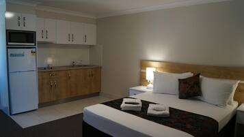 Habitación de hotel con cama, mesita de noche, lámpara y una zona de kitchenette con microondas y refrigerador.