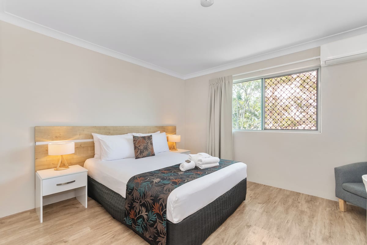 A hotel room with a bed, nightstands, a window with curtains, and a chair.