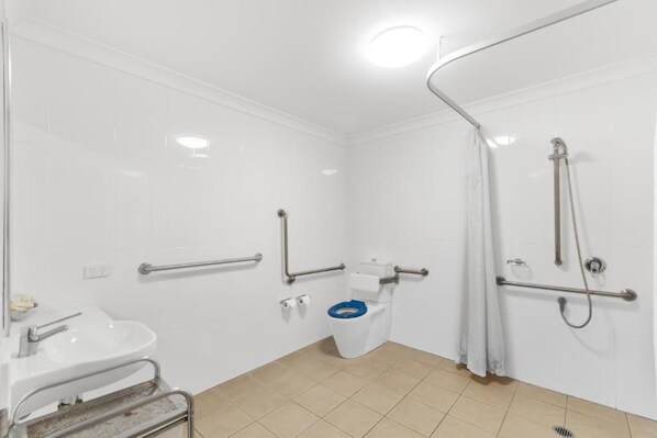A bathroom with white tiles, a white sink, a toilet with a blue seat, and a shower area.