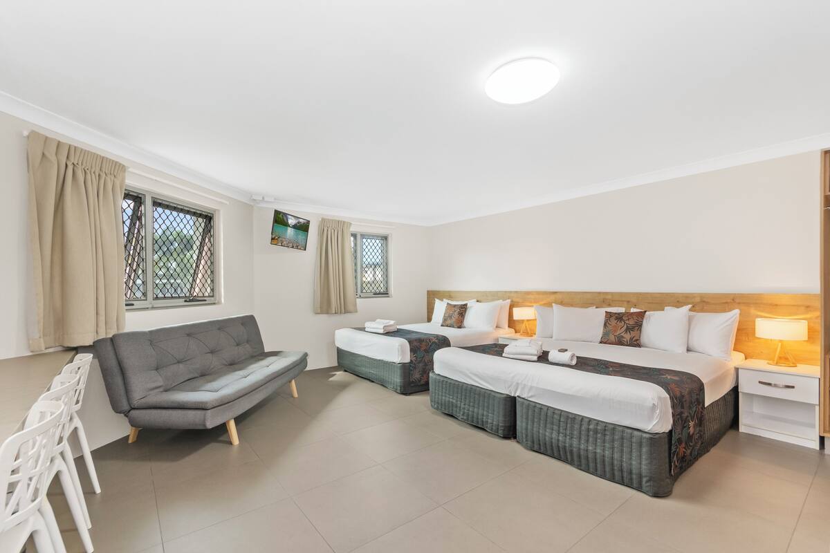 A hotel room with two single beds, a sofa, a desk, and a chair.