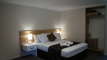 Une chambre d’hôtel avec un lit bien fait, une lampe de chevet, une tête de lit en bois et un placard intégré avec des étagères.