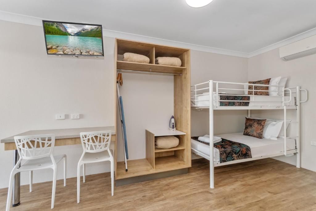 A bunk bed with a wooden shelf, a desk with two chairs, and a painting of a lake.