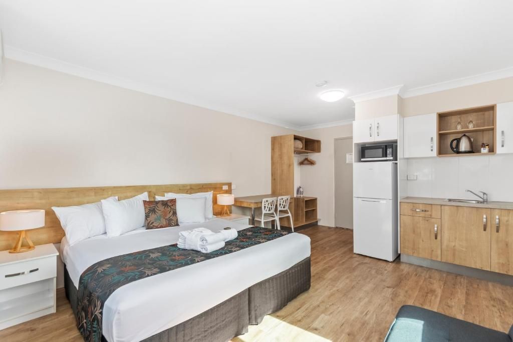 A hotel room with a bed, bedside table, lamp, and a kitchenette area with a microwave and refrigerator.