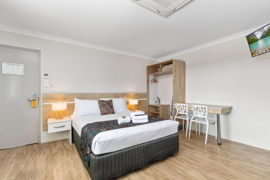 Ett hotellrum med en säng, ett sängbord, en lampa, ett skrivbord med stolar och en väggmonterad TV.