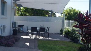 A patio with a table and chairs, air conditioning units, and a white fence. - Castle Crest Motel (North Ward)