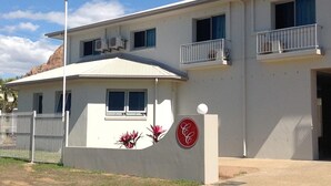 A two-story building with a white exterior, a balcony on the upper floor, and a red logo on the lower wall. - Castle Crest Motel (North Ward)