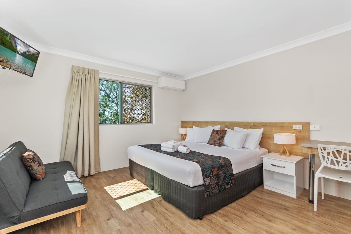 A hotel room with a bed, a sofa, a desk, and a TV mounted on the wall.