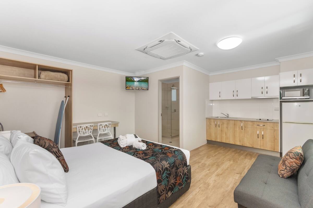 A modern hotel room with a bed, a sofa, a desk, and a kitchenette.