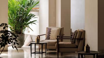 A spacious living area with a sofa, armchairs, and a coffee table. There is a large potted plant and a hanging light fixture.