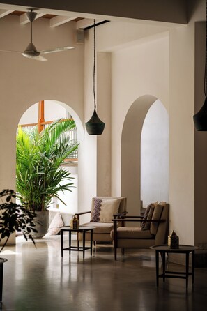 En rummelig opholdsstue med sofa, lænestole og sofabord. Der er en stor stueplante og en hængende lampe.