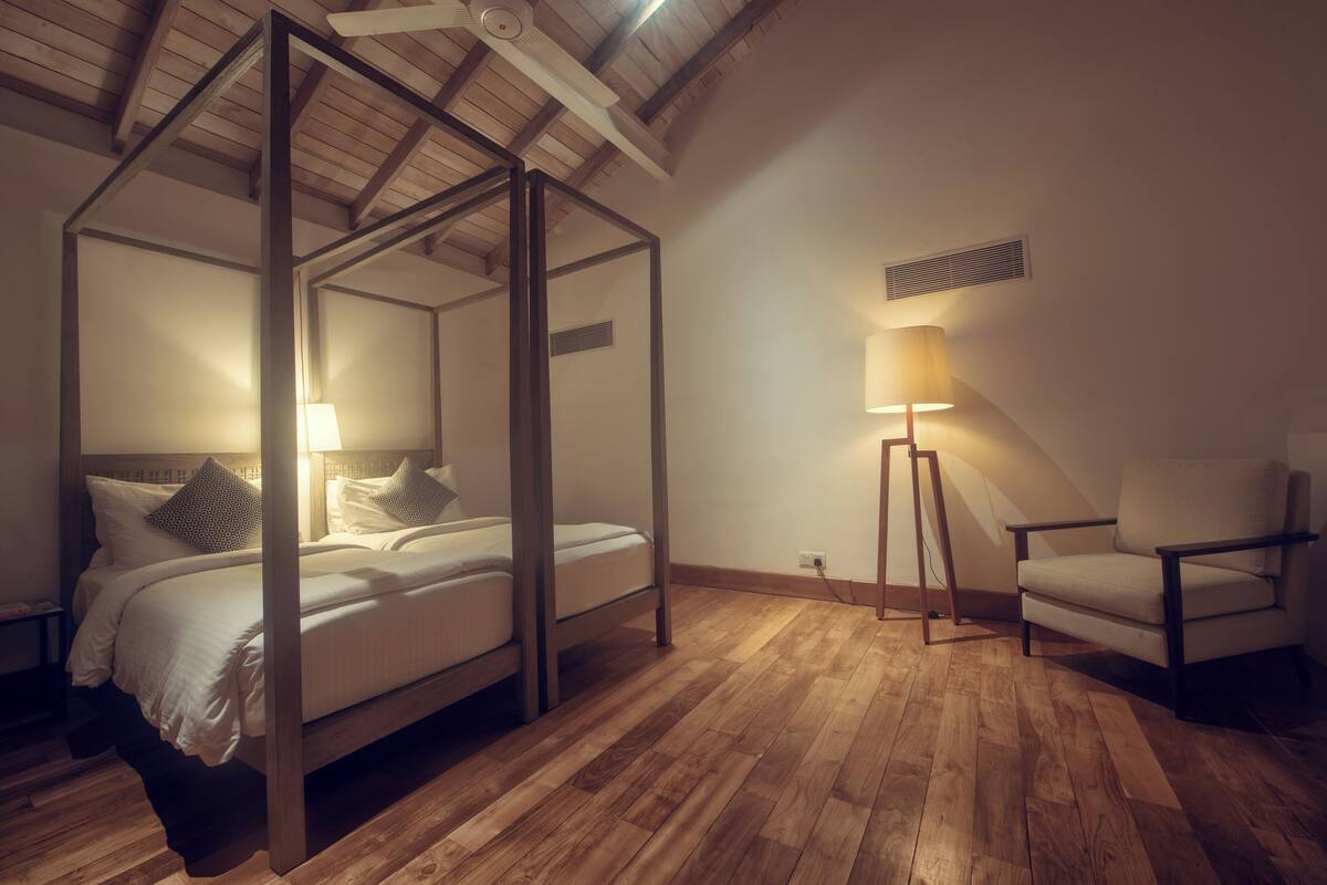 A four-poster bed with a lamp beside it in a room with wooden flooring and a sloped ceiling.