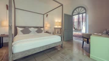 Una cama con dosel y almohadas estampadas, un escritorio con silla y una puerta que da a un espacio exterior.