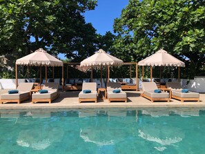 Un espace aménagé au bord de la piscine, avec des chaises longues et des parasols, entouré d’une végétation luxuriante.