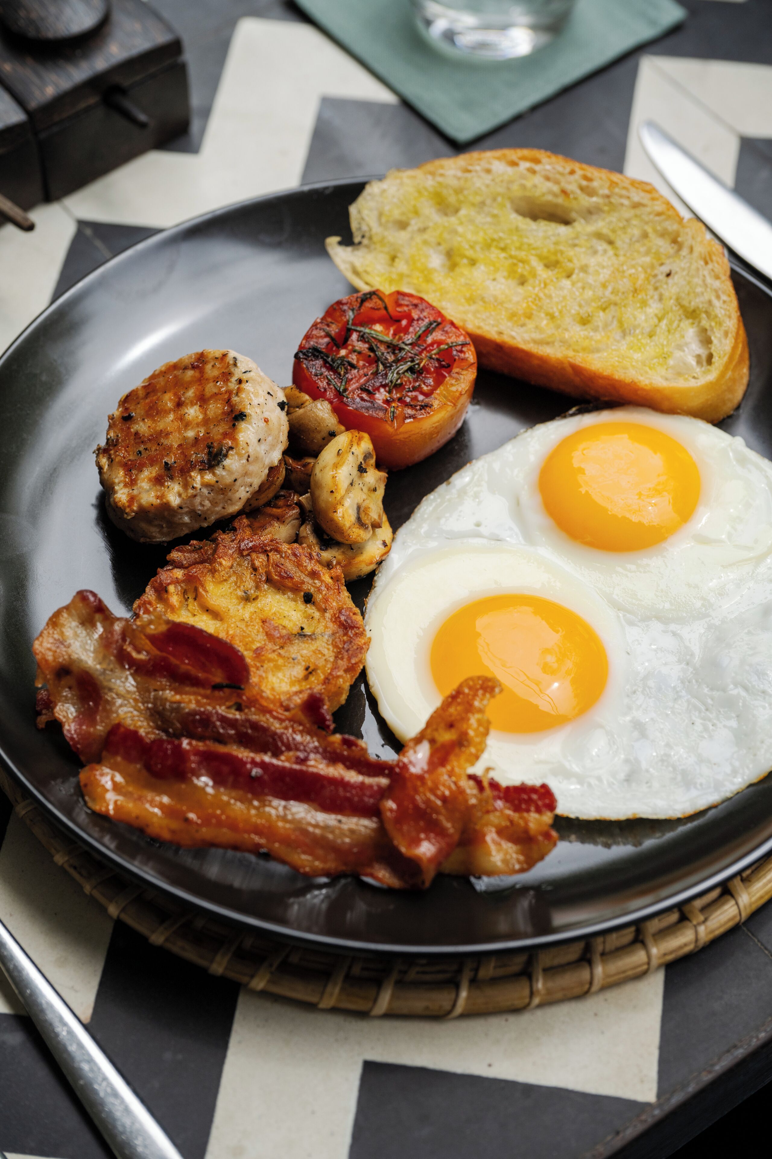 Ein Frühstücksteller mit Eiern, Speck, Pilzen, einer Tomate und Toast.