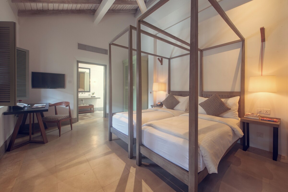 A four-poster bed with white linens, a bedside table with a lamp, and a television on the wall.
