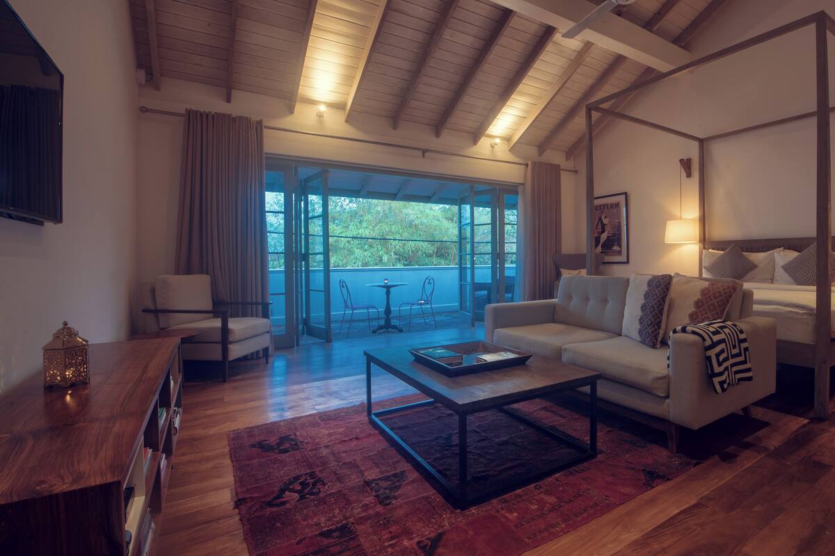 A spacious room with a four-poster bed, a sofa, a coffee table, and a view of the outdoors through large sliding doors.