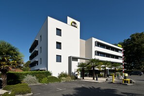 Un hotel moderno con un letrero de B&B, un estacionamiento y un cielo azul despejado.