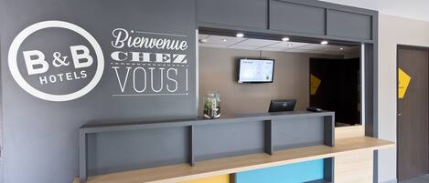 Una recepción con diseño moderno, una pantalla digital y un cartel que dice 'Bienvenue Chez Vous!'