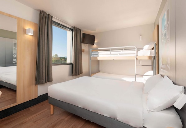 Habitación de hotel moderna con litera, cama doble, televisor y ventana con cortinas.