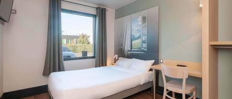 Una habitación de hotel con cama, una silla, un escritorio, un televisor y una ventana con cortinas.