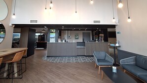 A modern reception area with a wooden reception desk, seating area with sofas and chairs, and hanging pendant lights. - B&B HOTEL La Rochelle Centre les Minimes (La Rochelle)