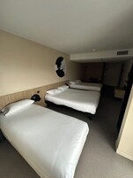 Habitación de hotel con tres camas individuales, cabecera de madera, una obra de arte en la pared y un pequeño escritorio con teléfono.