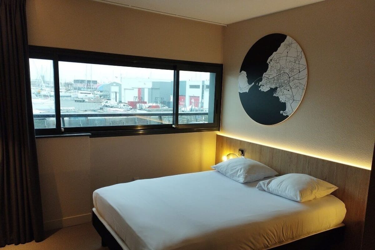 A hotel room with a large bed, a window with a view of the marina, and a wall-mounted map.
