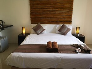 Una cama bien hecha con sábanas blancas y almohadas a rayas marrones, dos lámparas de noche y un escritorio pequeño con una lámpara.