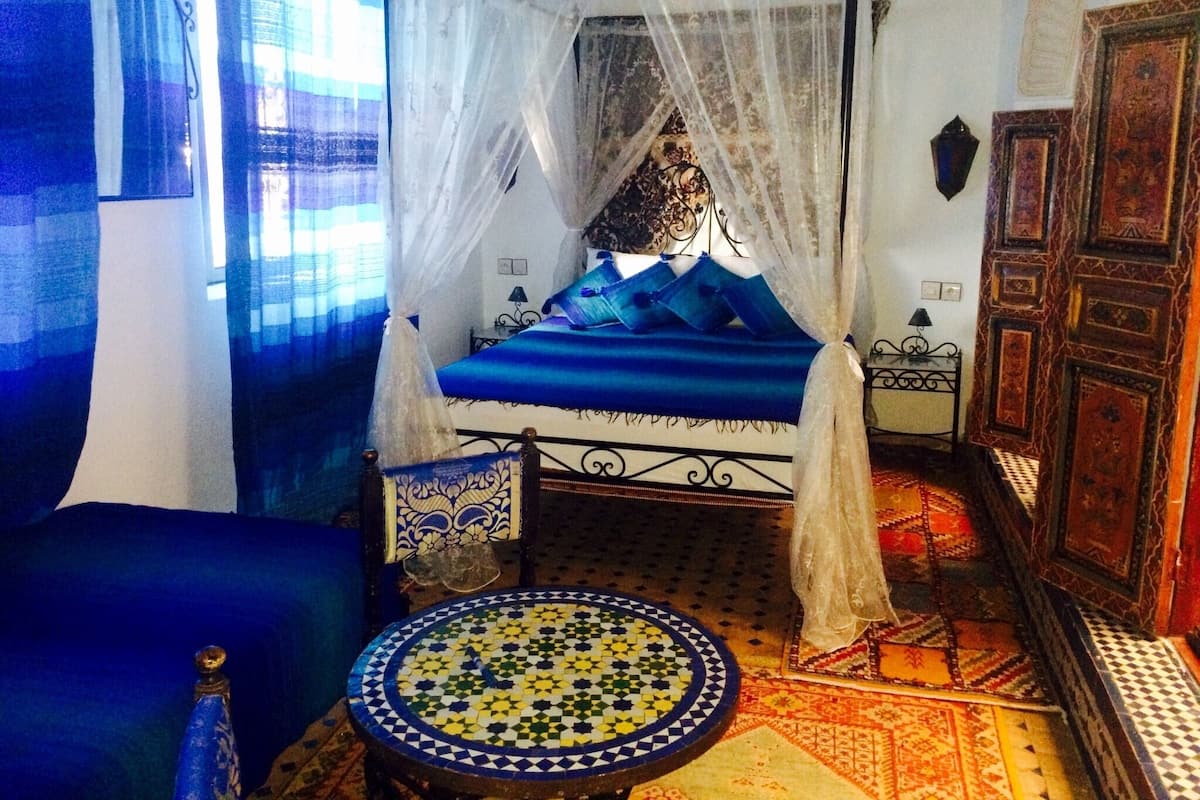 Um quarto com uma cama, uma mesa pequena e um guarda-roupa.