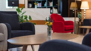 Un vestíbulo moderno con sofás oscuros, un sillón rojo y una mesa de centro de madera con un jarrón de flores amarillas.
