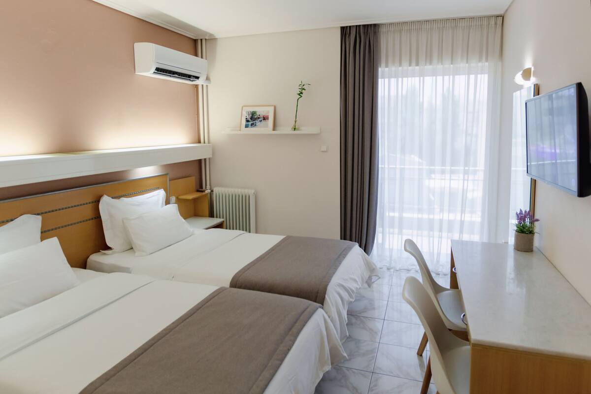 A hotel room with two beds, a desk, a chair, a television, and a window with curtains.
